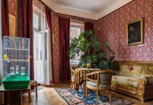 Svetainė su sofa ir paukščių narveliu prie lango